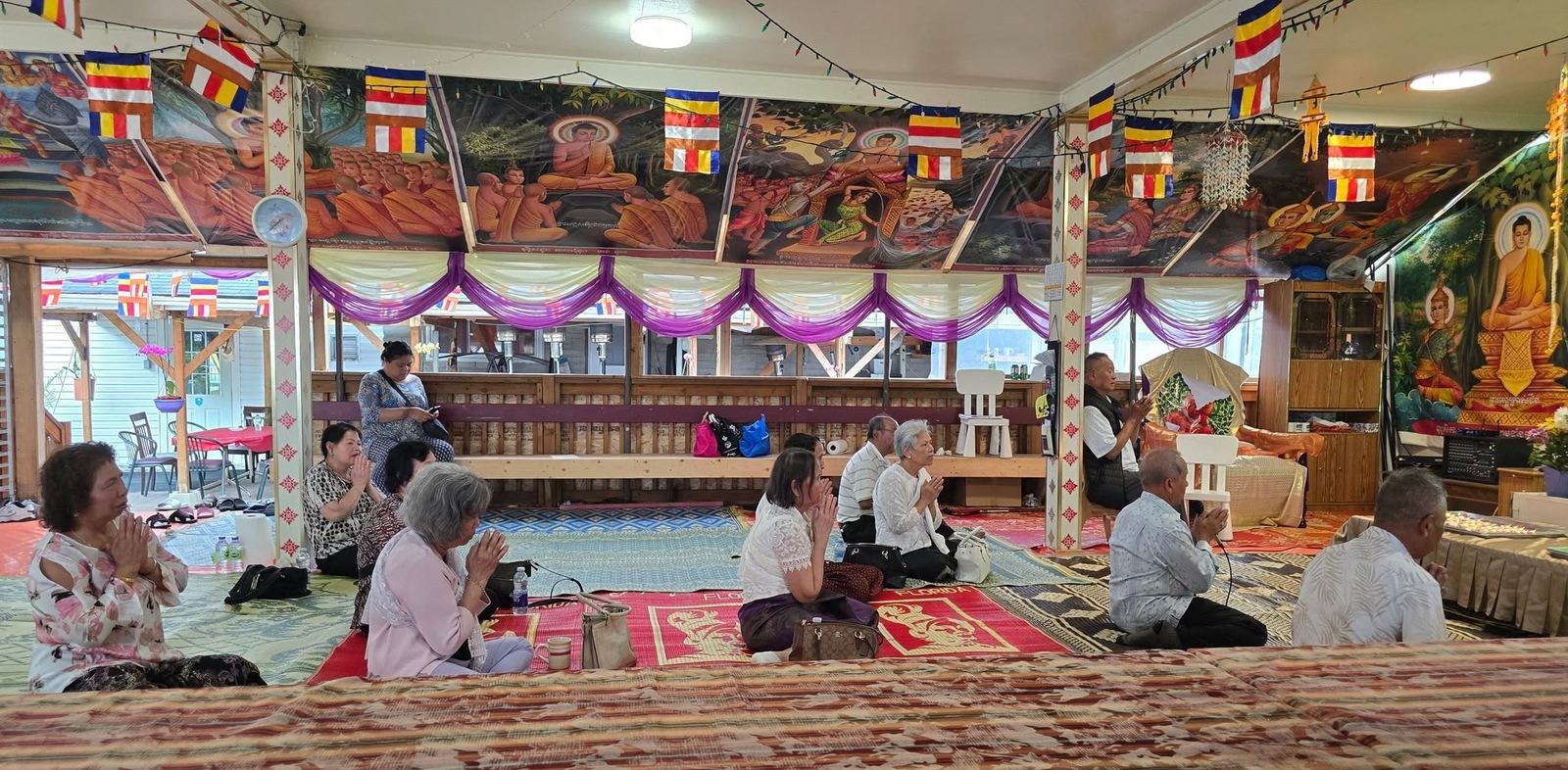 People praying on red carpets in the temple hall, under strings of Buddhist flags and painted murals