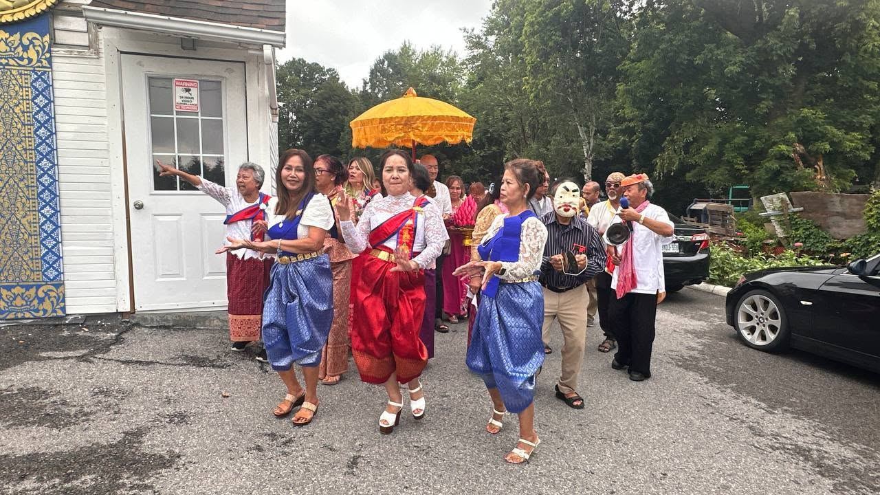 Women dancing in blue and red silk, leading a procession under a golden umbrella