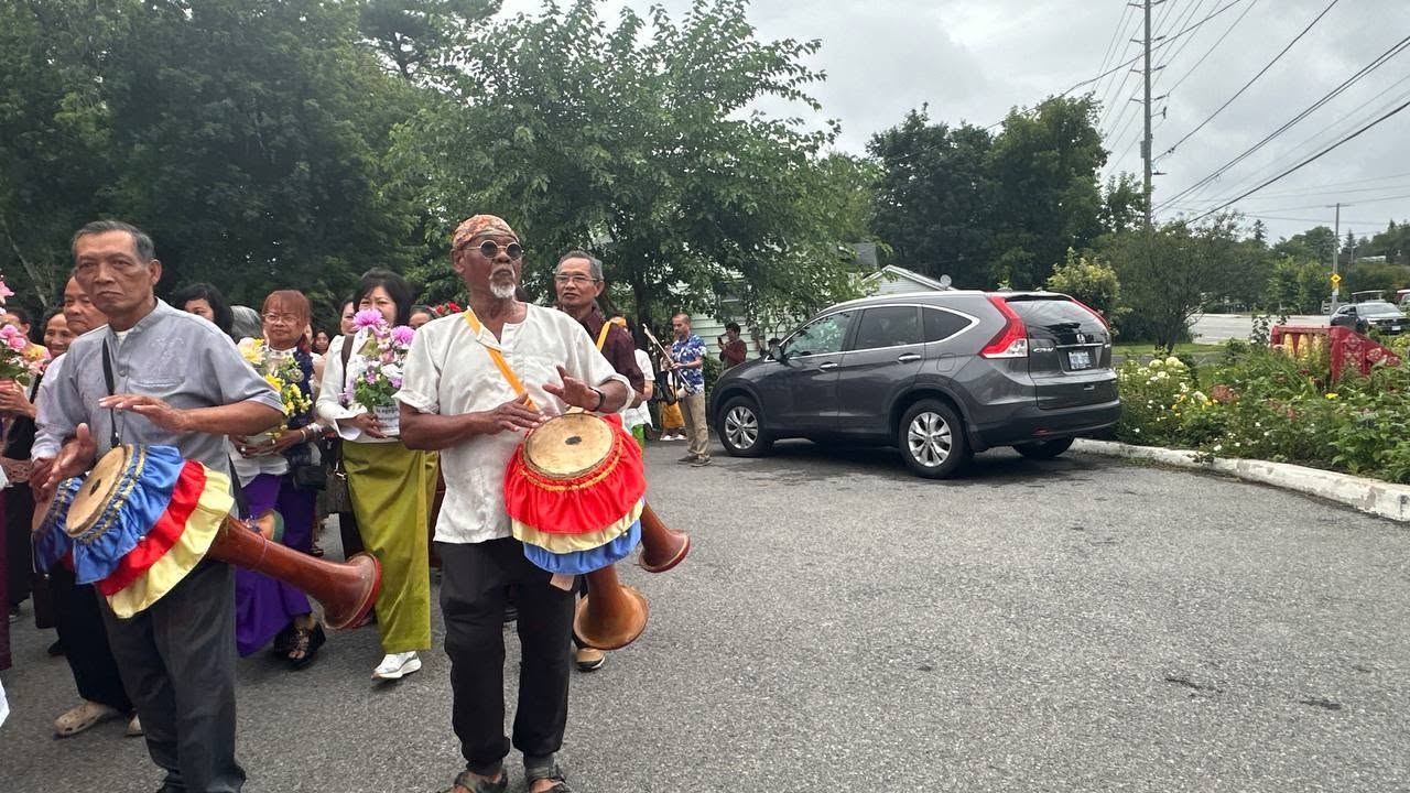 Two men playing traditional drums as the procession passes through the car park