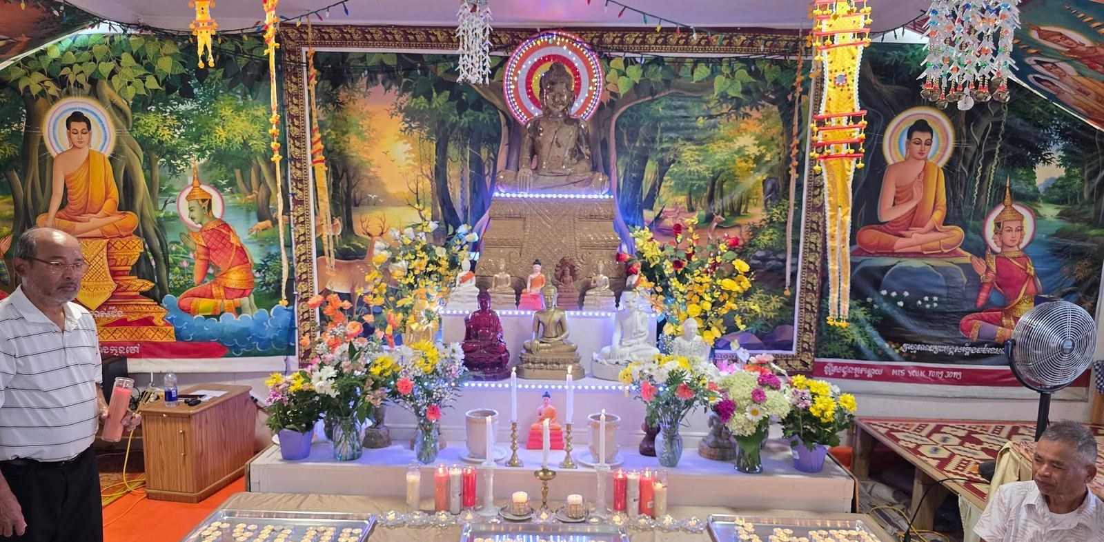 The shrine room, with a Buddha statue, fresh flowers, candles and painted murals of the Buddha